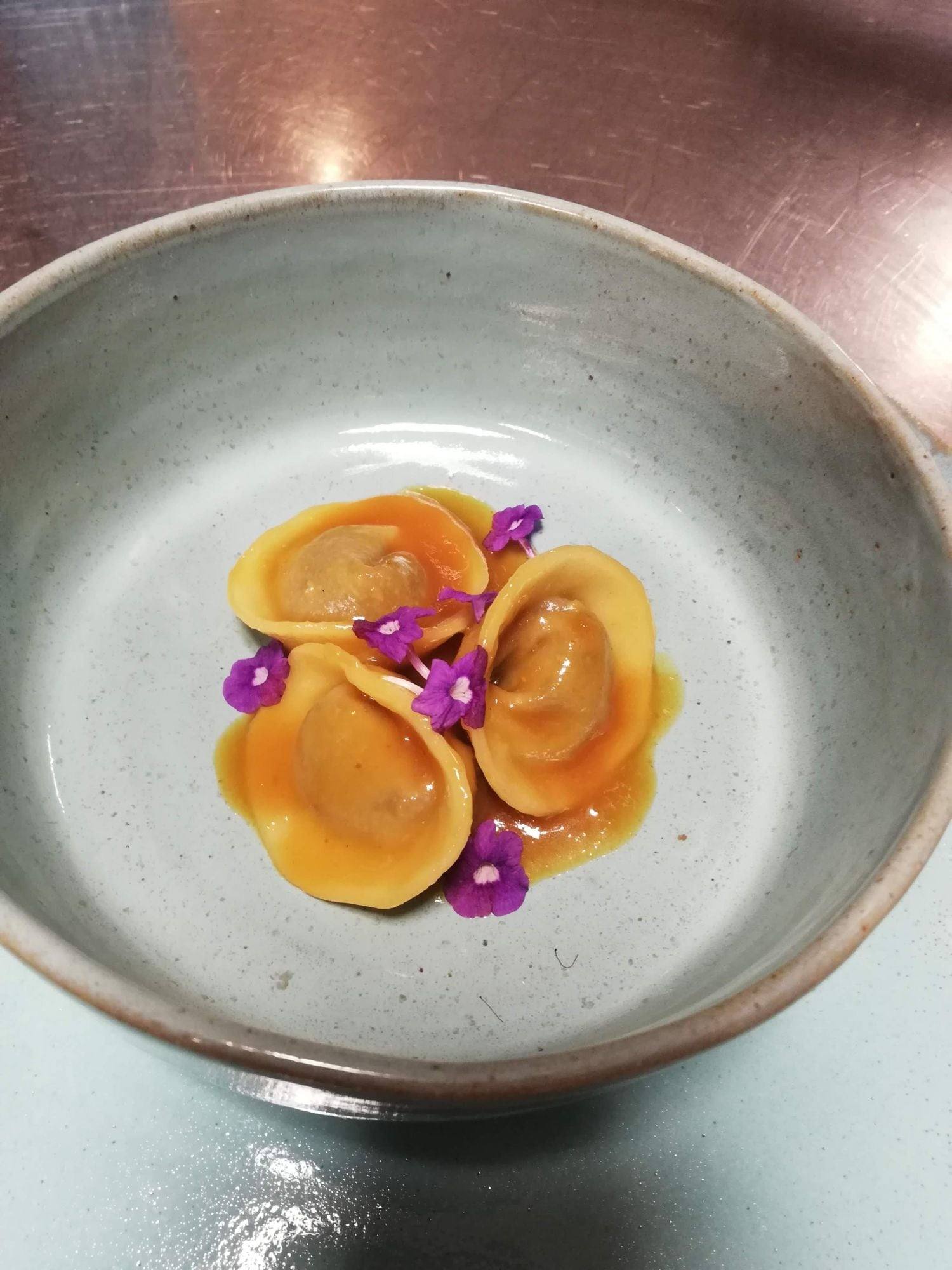Pasta rellena hecha a mano en salsa dorada con flores comestibles