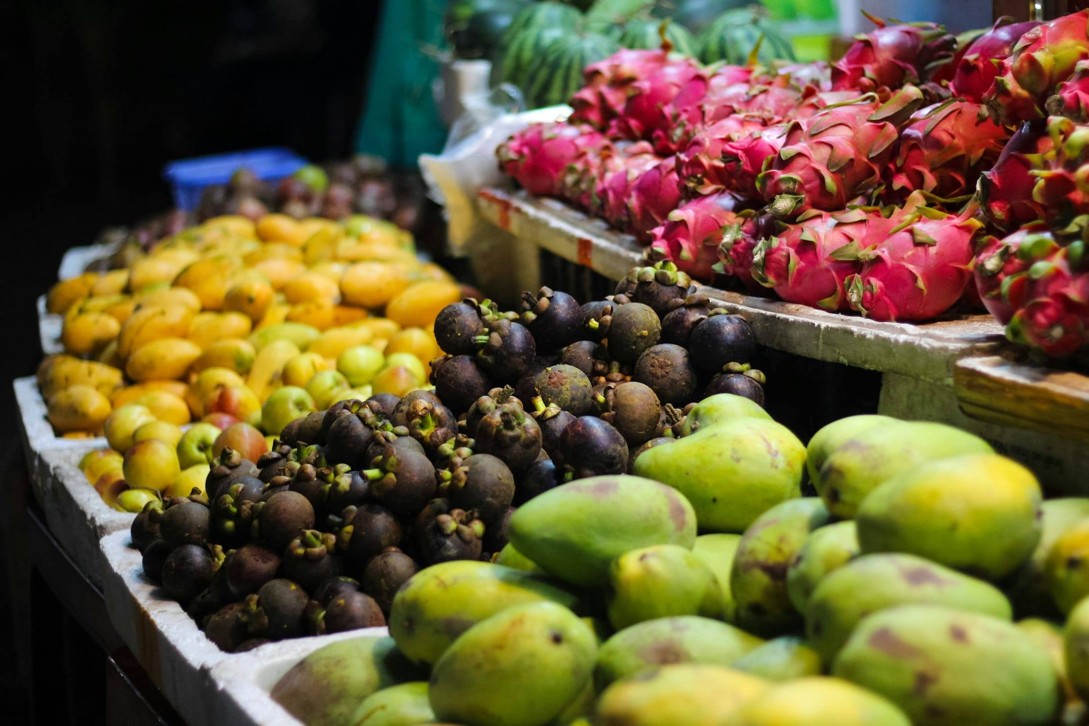 Puesto de mercado con mangos, pitahayas y productos tropicales
